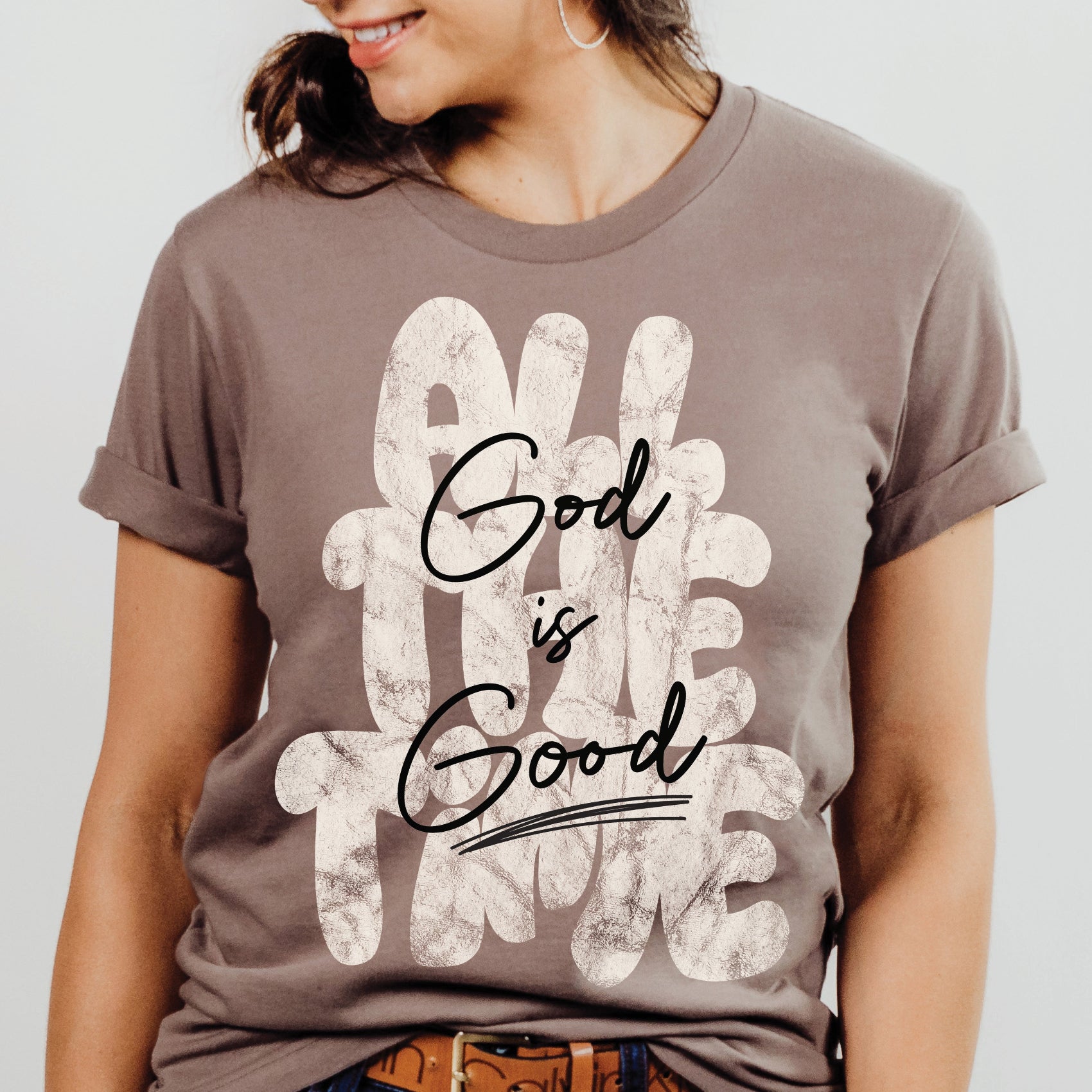 Woman wearing a Christian faith-based unisex pebble taupe brown t-shirt with inspirational quote 'God is Good All The Time' in modern trendy font – religious apparel for men and women
