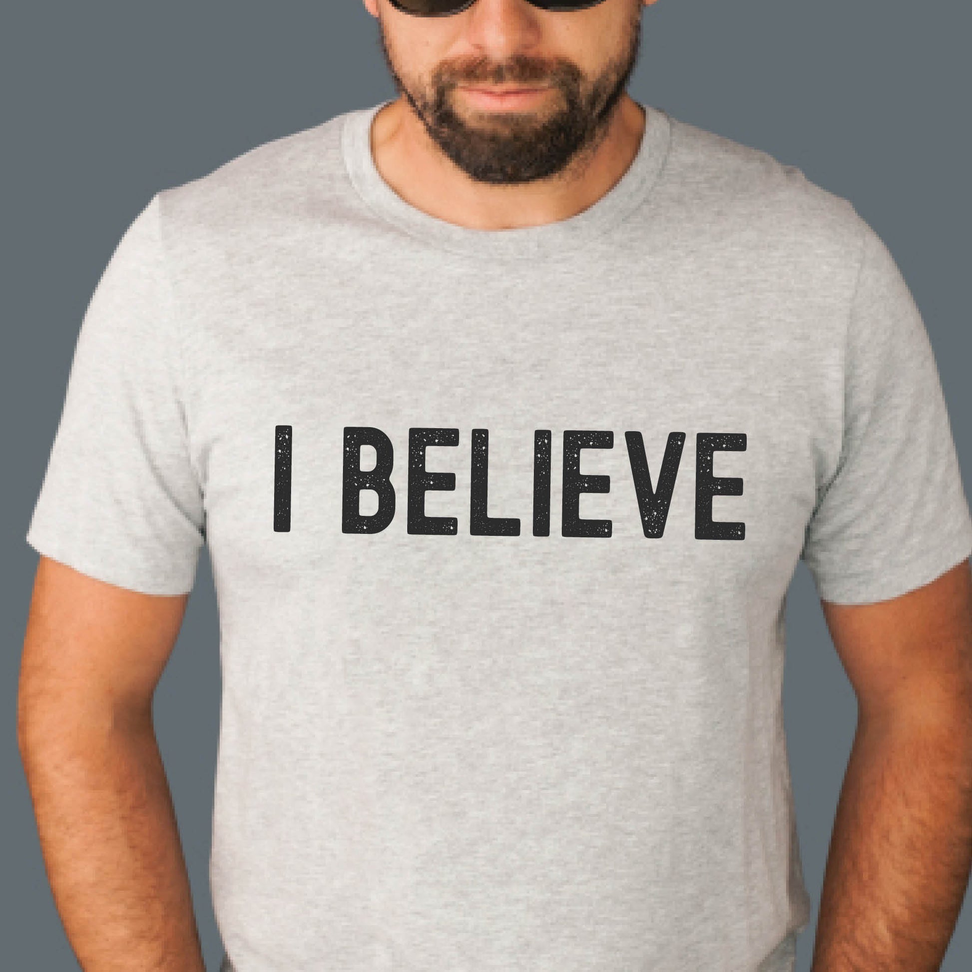 Man or Dad wearing an I BELIEVE Christian aesthetic faith-based bold statement distressed typography t-shirt design printed in matte black on sport gray unisex fit t-shirt, designed for men & women believers