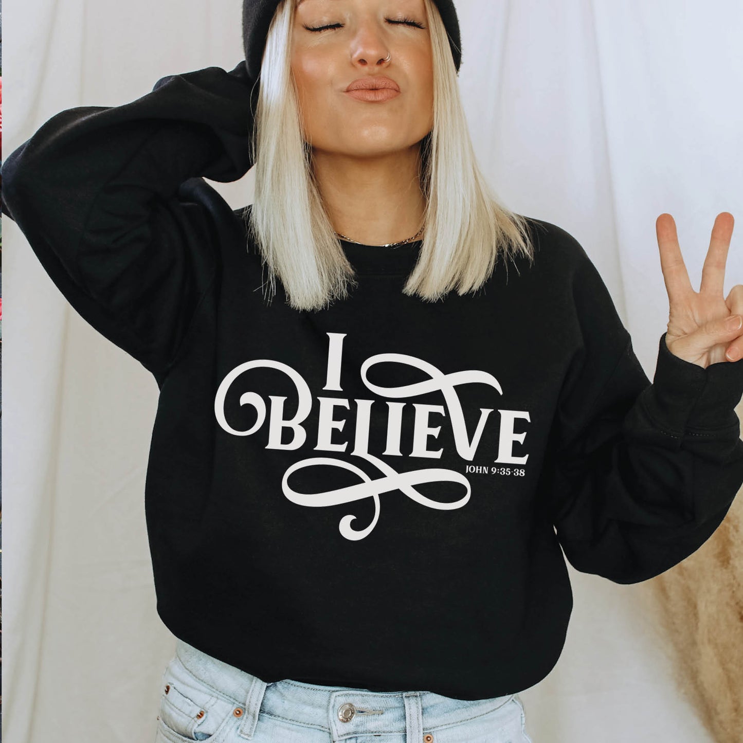 Young woman wearing a black I BELIEVE John 9:35-38 bible verse women's Christian unisex cozy sweatshirt, designed for faith-filled Jesus believers in size small, medium, large, XL, 2XL, 3XL, 4XL