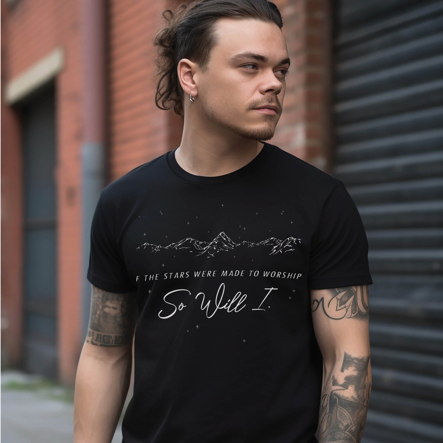 Young Christian man wearing a black color garment-dyed unisex Comfort Colors 1717 t-shirt with white hand-drawn mountain range and starry sky that says this faith-based bible verse quote, "If the Stars Were Made to Worship So Will I", created for Christian men and women Kingdom believers