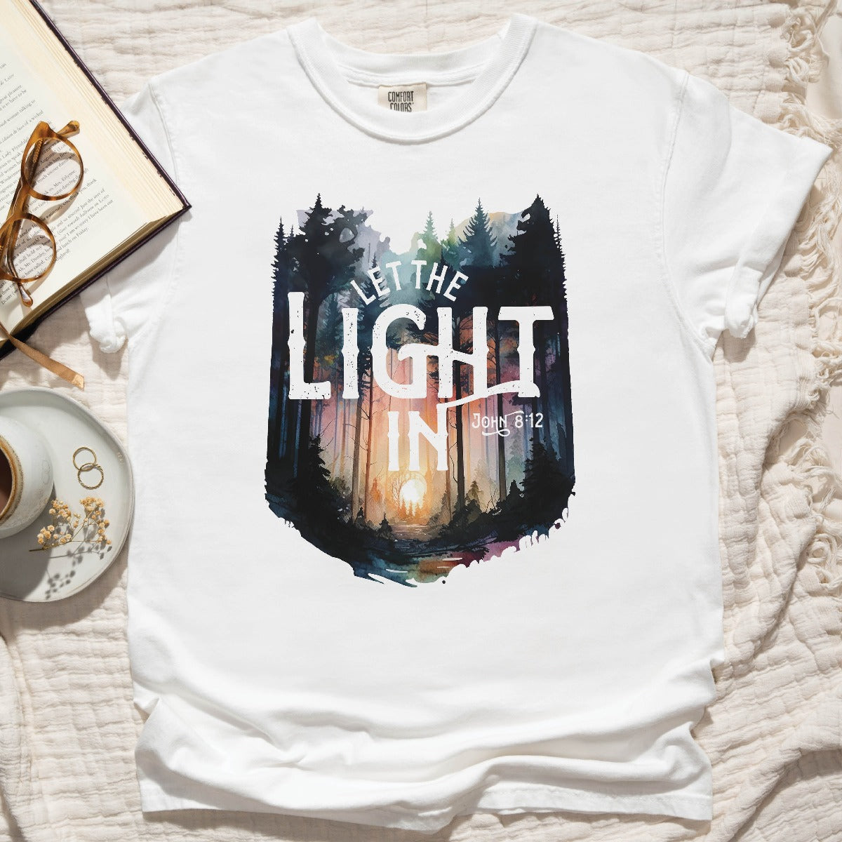White Comfort Colors C1717 unisex faith-based Christian t-shirt with "Let the Light In" John 8:12 bible verse and watercolor moody forest trees scene, designed for men and women