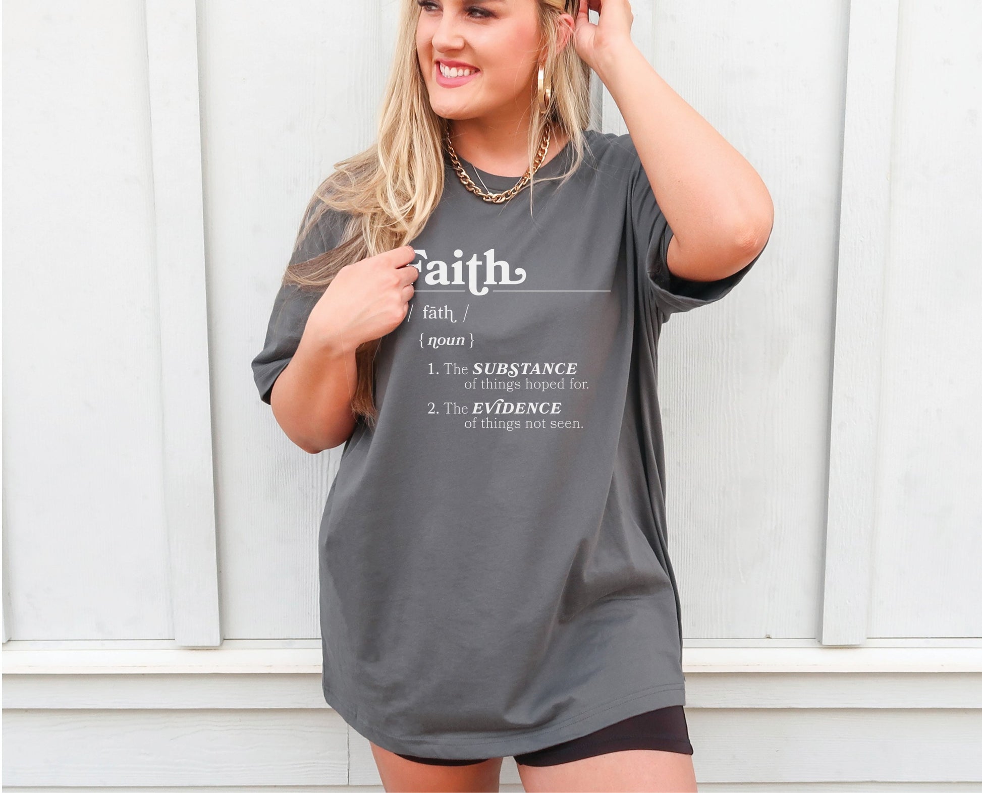 Young woman wearing a Faith Definition Hebrews 11:1 Christian aesthetic design printed in white on soft oversized asphalt gray unisex t-shirt for women and men