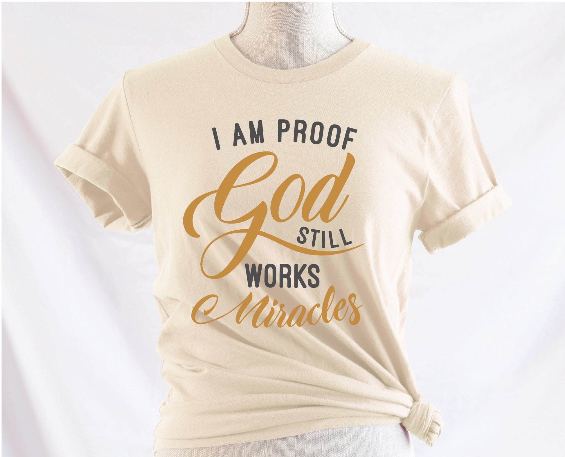 I am proof God still works miracles Christian aesthetic testimony design printed in charcoal and gold on soft cream unisex t-shirt for women