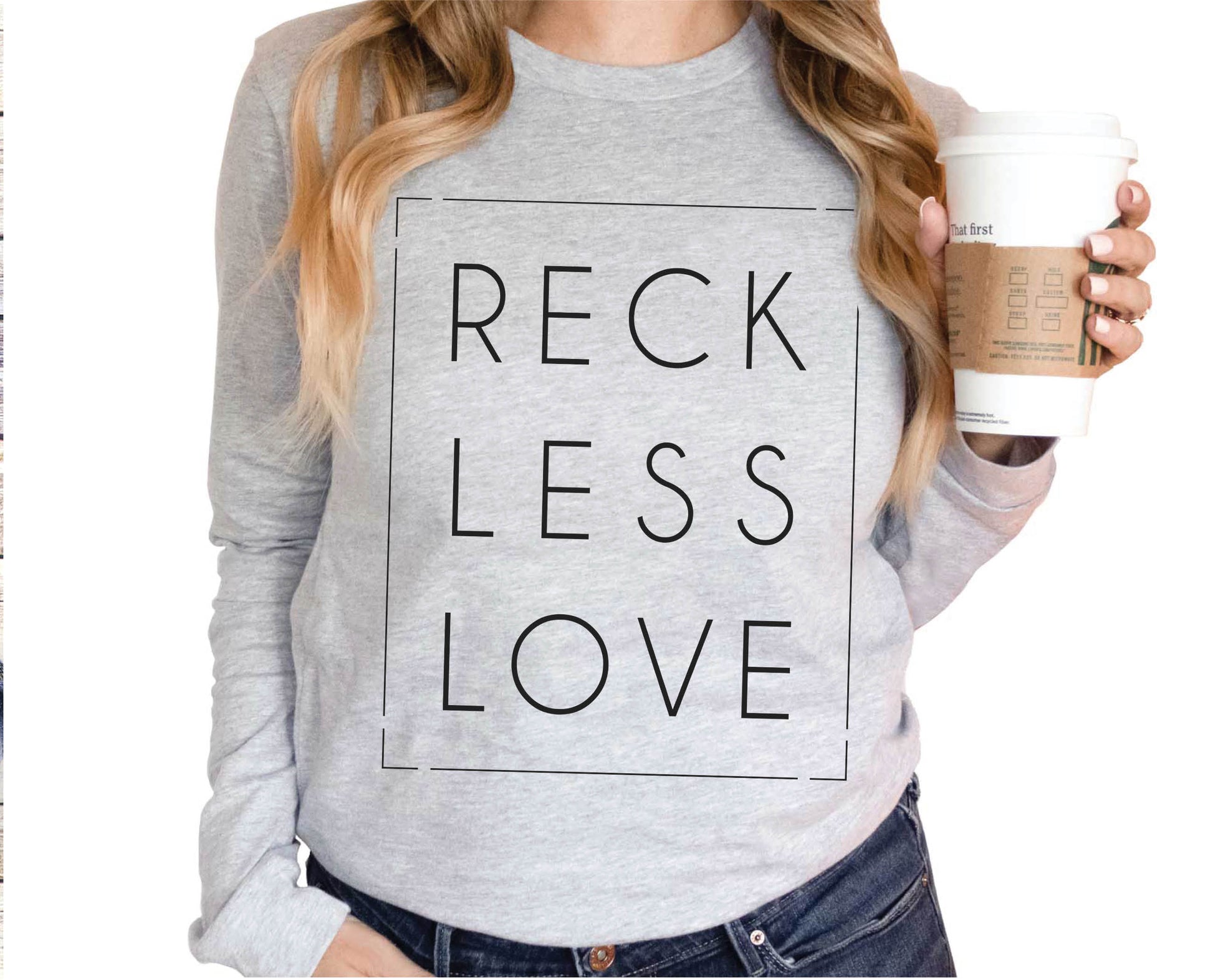 Woman holding Coffee wearing a Rectangle Reckless Love Christian aesthetic worship design printed in black on cozy white unisex long sleeve tee shirt for men and women
