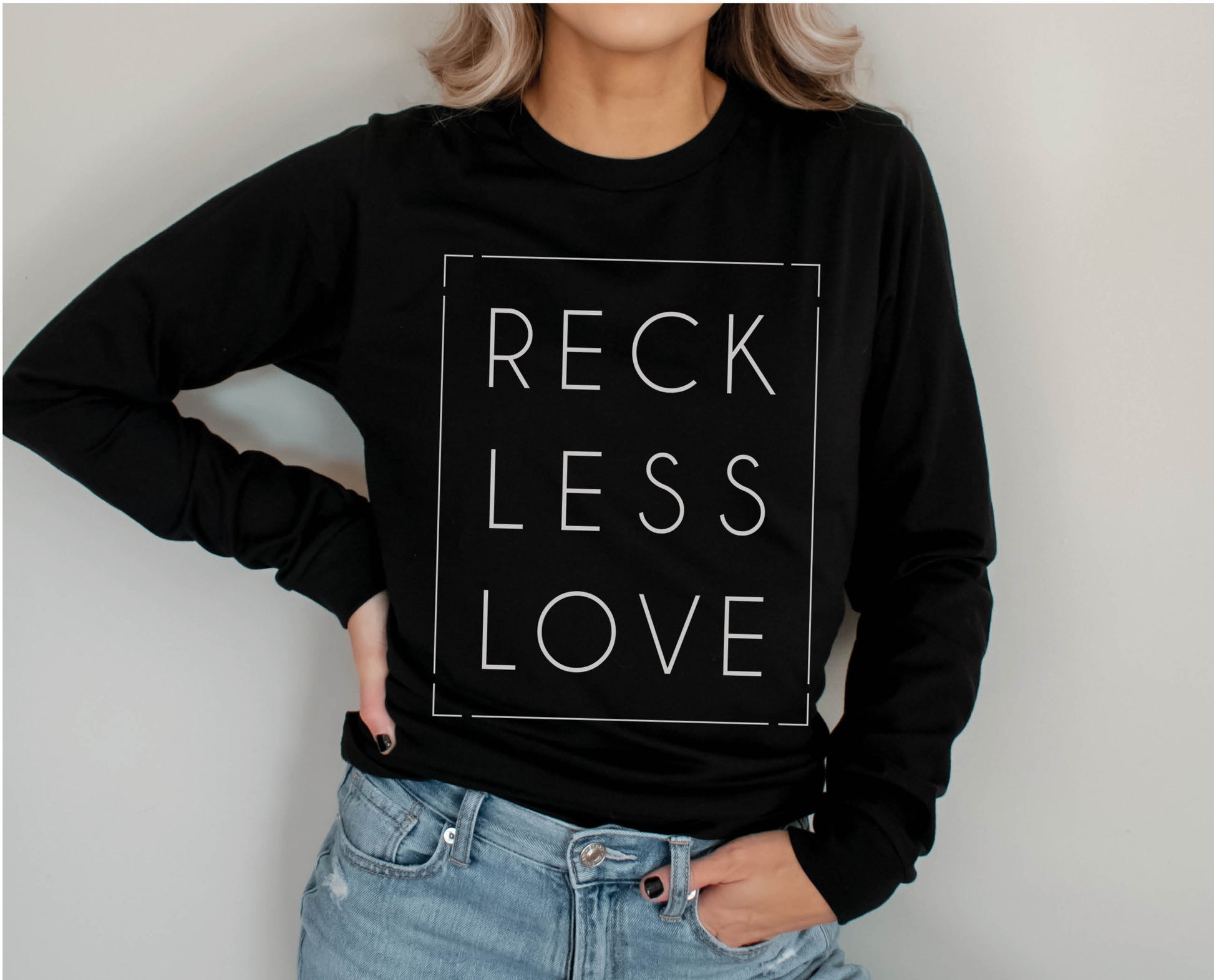 Trendy woman wearing a Rectangle Reckless Love Christian aesthetic worship design printed in white on cozy black unisex long sleeve tee shirt for men and women