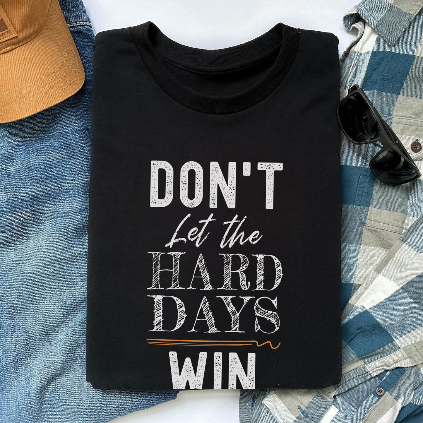 Black men's unisex Christian t-shirt with a bold typography design that says, "Don't Let The Hard Days Win" printed on the front in white and orange