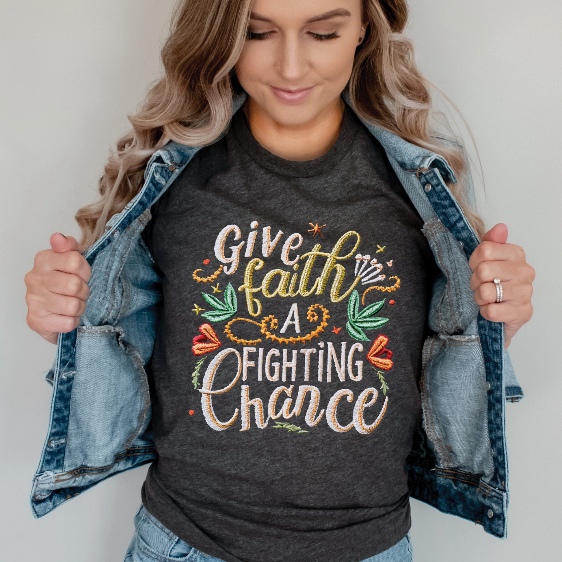 Trendy young woman wearing a heather dark gray t-shirt with printed embroidery font Christian Bible verse quote that says, "Give Faith A Fighting Chance" with flower and leaf graphics, faith-based t-shirt designed for women