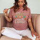 Trendy young woman wearing a mauve dusty rose t-shirt with printed embroidery font Christian Bible verse quote that says, "Give Faith A Fighting Chance" with flower and leaf graphics, faith-based t-shirt designed for women