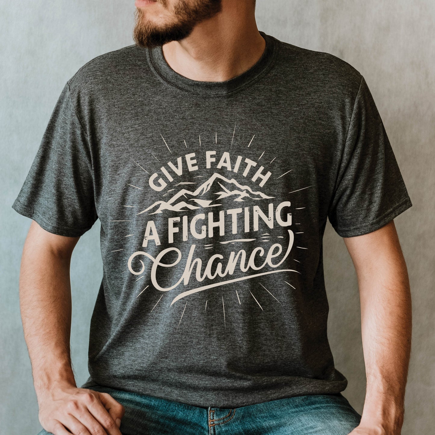 Bearded Man wearing a Heather Dark Gray Unisex Tee with Christian Bible verse quote that says, "Give Faith A Fighting Chance" with retro sunburst and mountain graphics, designed for faith-based men and women