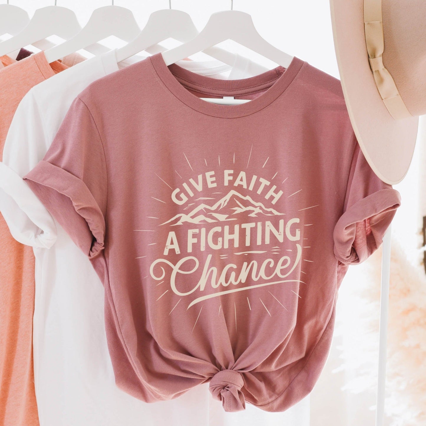 Trendy Mauve pink Unisex Tee with Christian Bible verse quote that says, "Give Faith A Fighting Chance" with retro sunburst and mountain graphics, t-shirt designed for faith-based men and women