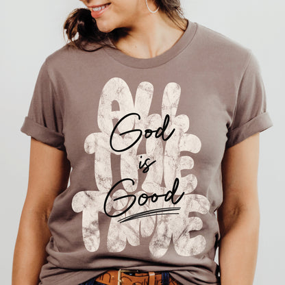 Woman wearing a Christian faith-based unisex pebble taupe brown t-shirt with inspirational quote 'God is Good All The Time' in modern trendy font – religious apparel for men and women