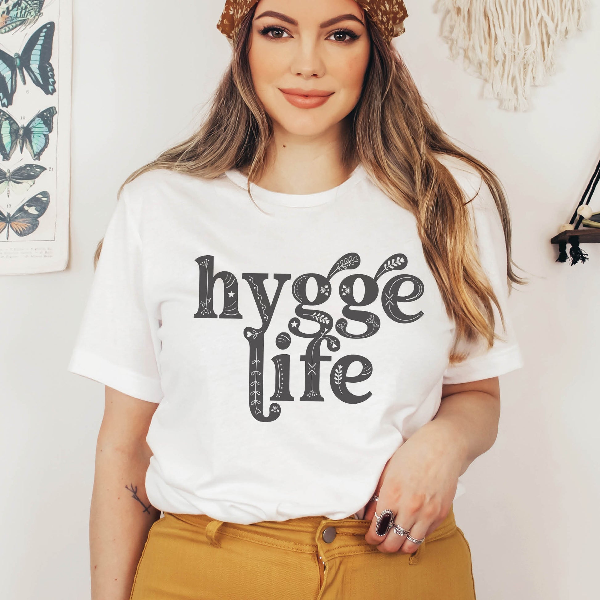Coziness vibes boho woman wearing a white and gray Hygge Life Holy Hygge Women's unisex Christian t-shirt with Scandinavian floral and heart art for the cozy fall and winter season