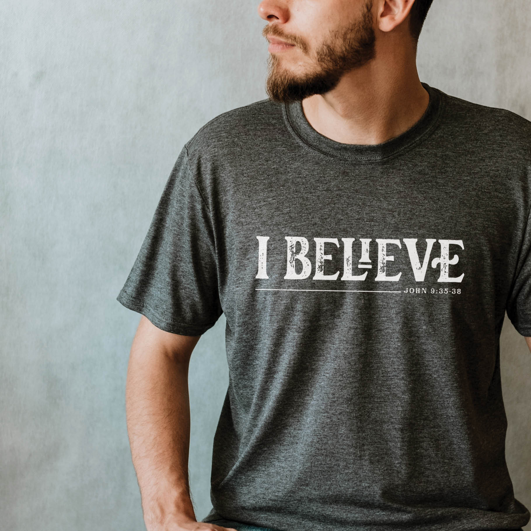 Young bearded man believer with a wearing a heather dark gray I BELIEVE John 9:35-38 bible verse faith statement Men's Christian black t-shirt, "I was blind and now I see" scripture