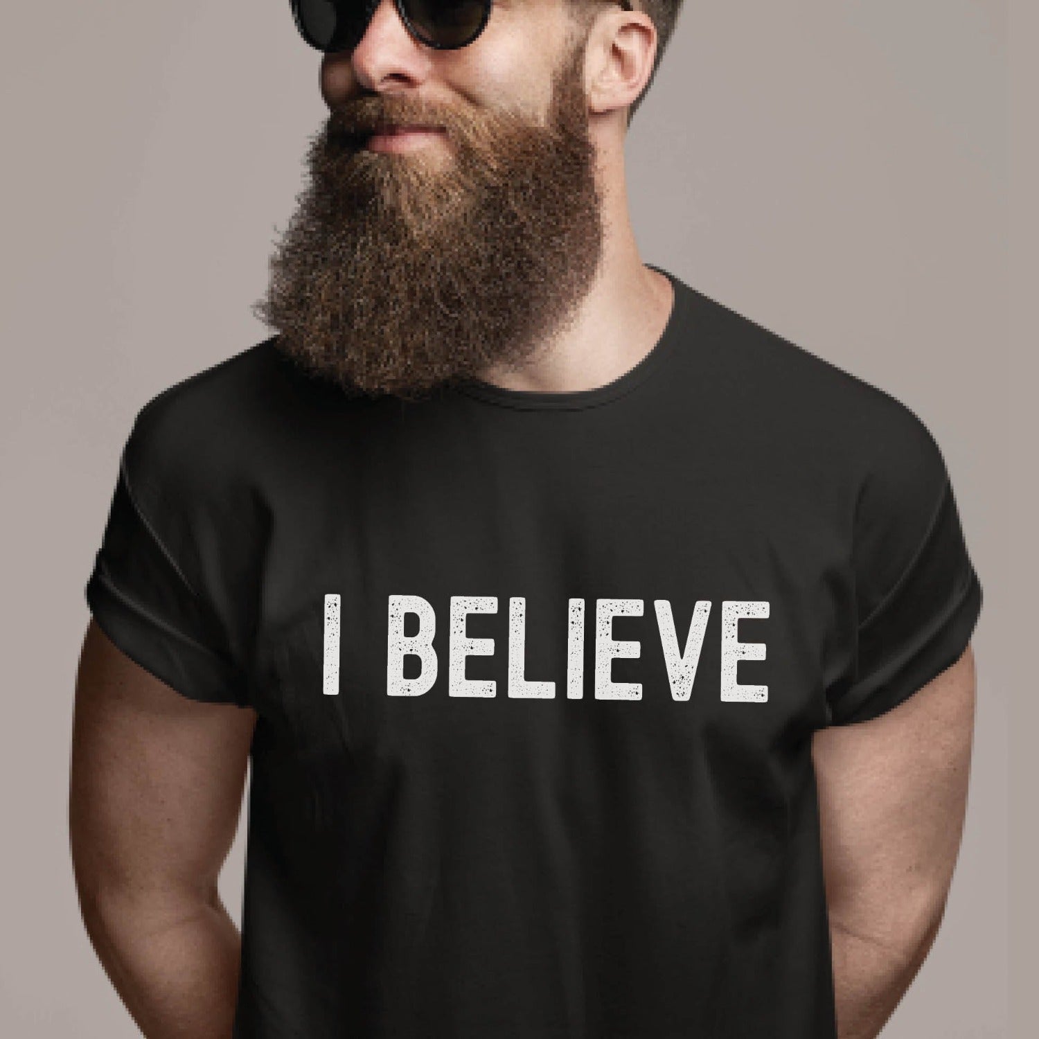 Trendy bearded man with sunglasses wearing an I BELIEVE Christian aesthetic faith-based bold statement distressed typography t-shirt design printed in white on soft black unisex fit t-shirt, designed for men & women believers