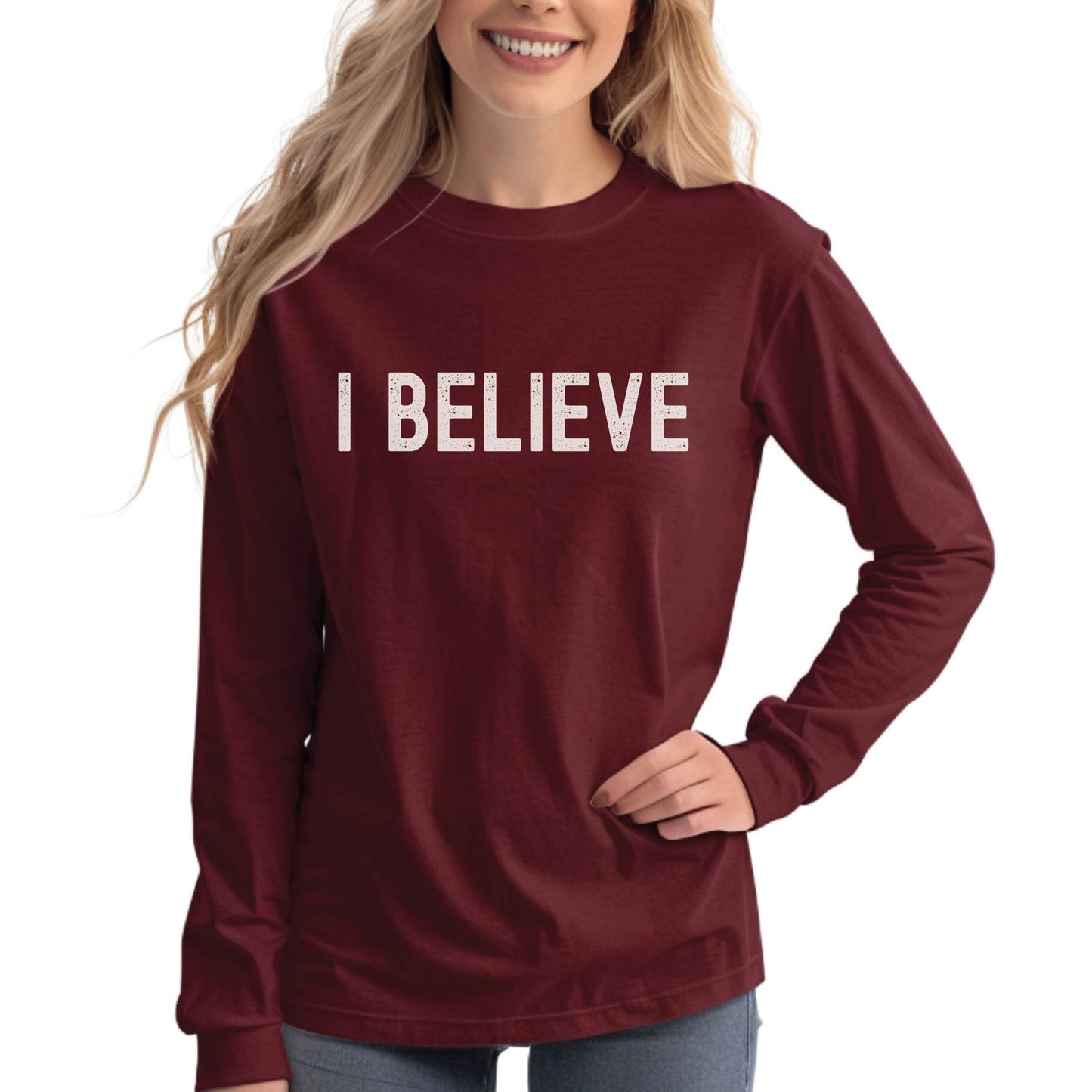 Young woman wearing a maroon burgundy cozy long sleeve t-shirt with a bold faith-based statement "I BELIEVE" distressed typography design printed in white, created for Christian men and women Jesus believers