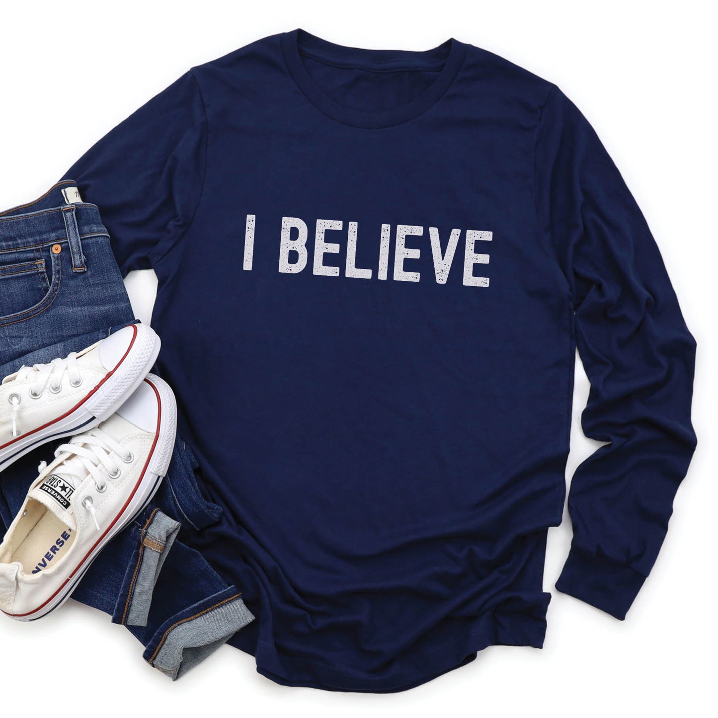 Navy blue cozy long sleeve t-shirt with a bold faith-based statement "I BELIEVE" distressed typography design printed in white, created for Christian men and women Jesus believers