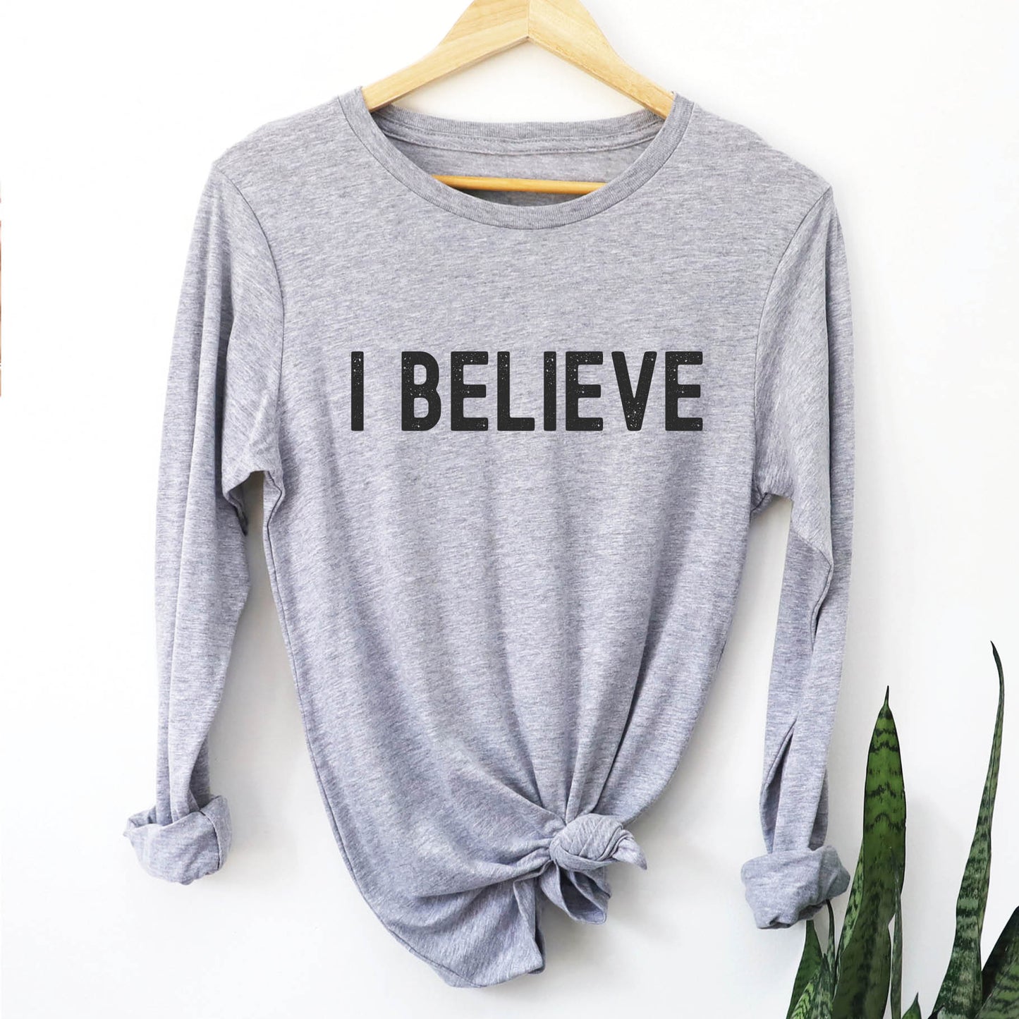 Heather sport gray cozy long sleeve t-shirt with a bold faith-based statement "I BELIEVE" distressed typography design printed in black, created for Christian men and women Jesus believers