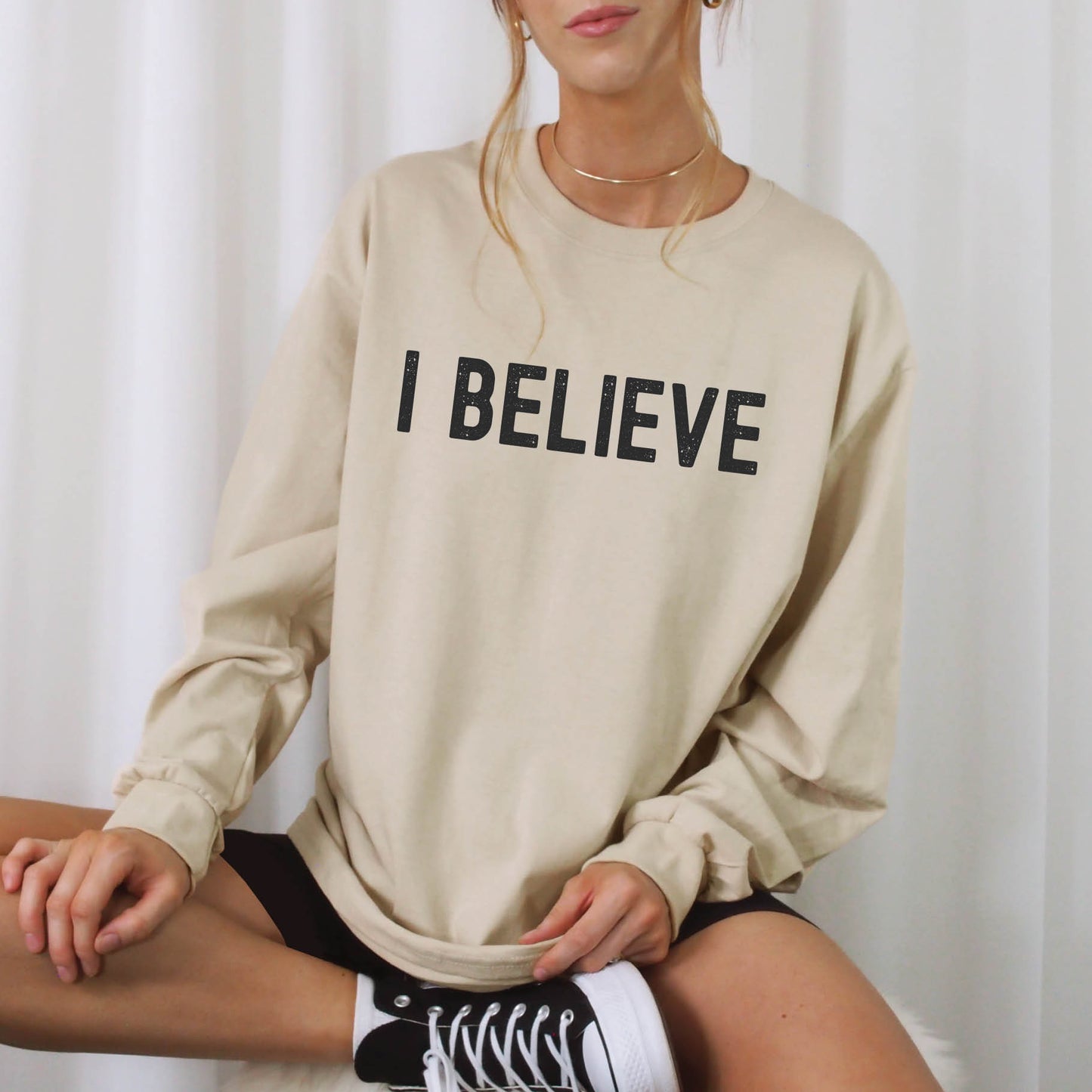 Sand beige color cozy long sleeve t-shirt with a bold faith-based statement "I BELIEVE" distressed typography design printed in black, created for Christian men and women Jesus believers