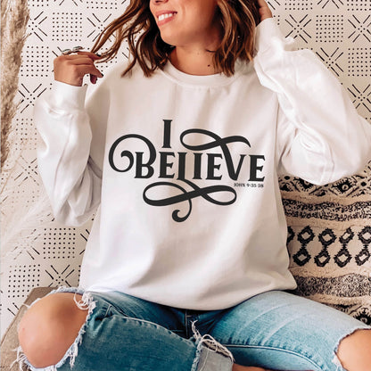 Young woman wearing a white I BELIEVE John 9:35-38 bible verse women's Christian unisex cozy sweatshirt, designed for faith-filled Jesus believers in size small, medium, large, XL, 2XL, 3XL, 4XL