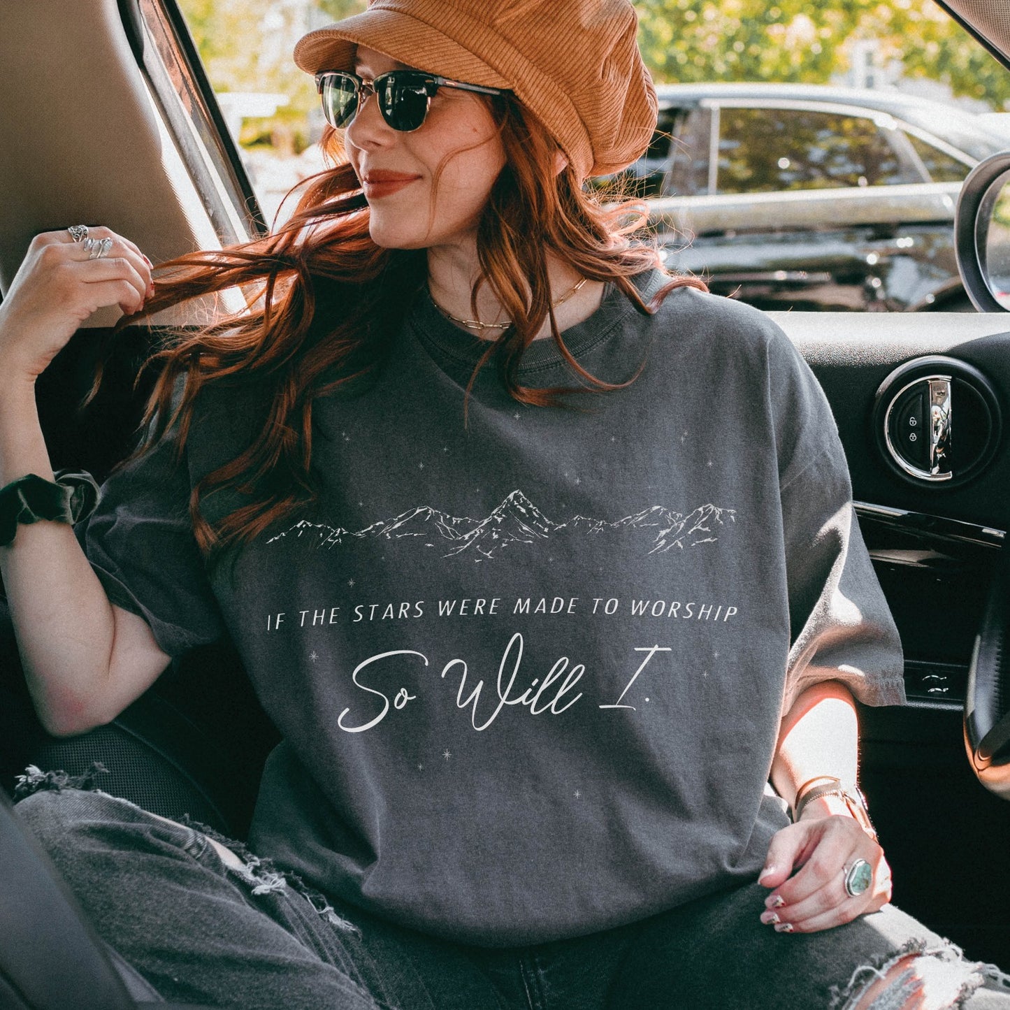 Trendy young woman wearing a Pepper color garment-dyed unisex Comfort Colors 1717 t-shirt a white hand-drawn mountain range and starry sky that says this faith-based bible verse quote, "If the Stars Were Made to Worship So Will I", created for Christian men and women Kingdom believers