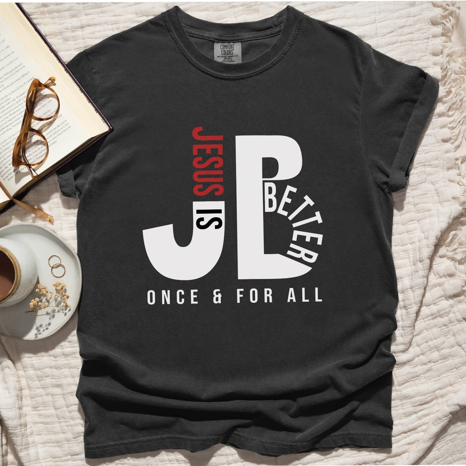 "JB" typography "Jesus is Better Once and For All" design in white and red, Christian, based on the bible book of Hebrews, printed on a Pepper dark gray color Unisex Comfort Colors C1717 t-shirt, with Jesus in red letters, created for faith-based women and men