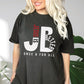 Trendy woman wearing a "JB" typography "Jesus is Better Once and For All" design in white and red, Christian, based on the bible book of Hebrews, printed on a Pepper dark gray color Unisex Comfort Colors C1717 t-shirt, with Jesus in red letters, created for faith-based women and men