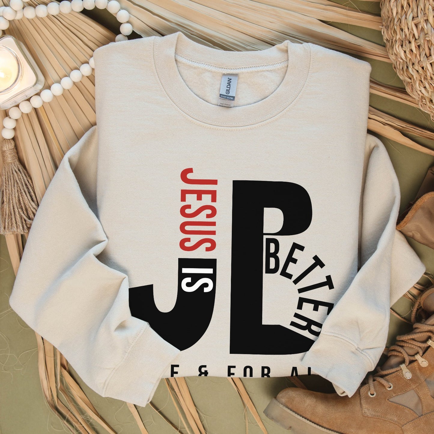 Cozy "JB" typography "Jesus is Better Once and For All" design in black and red letters, based on the Christian bible book of Hebrews, printed on a sand ivory color Unisex crewneck sweatshirt, created for faith-based men and women
