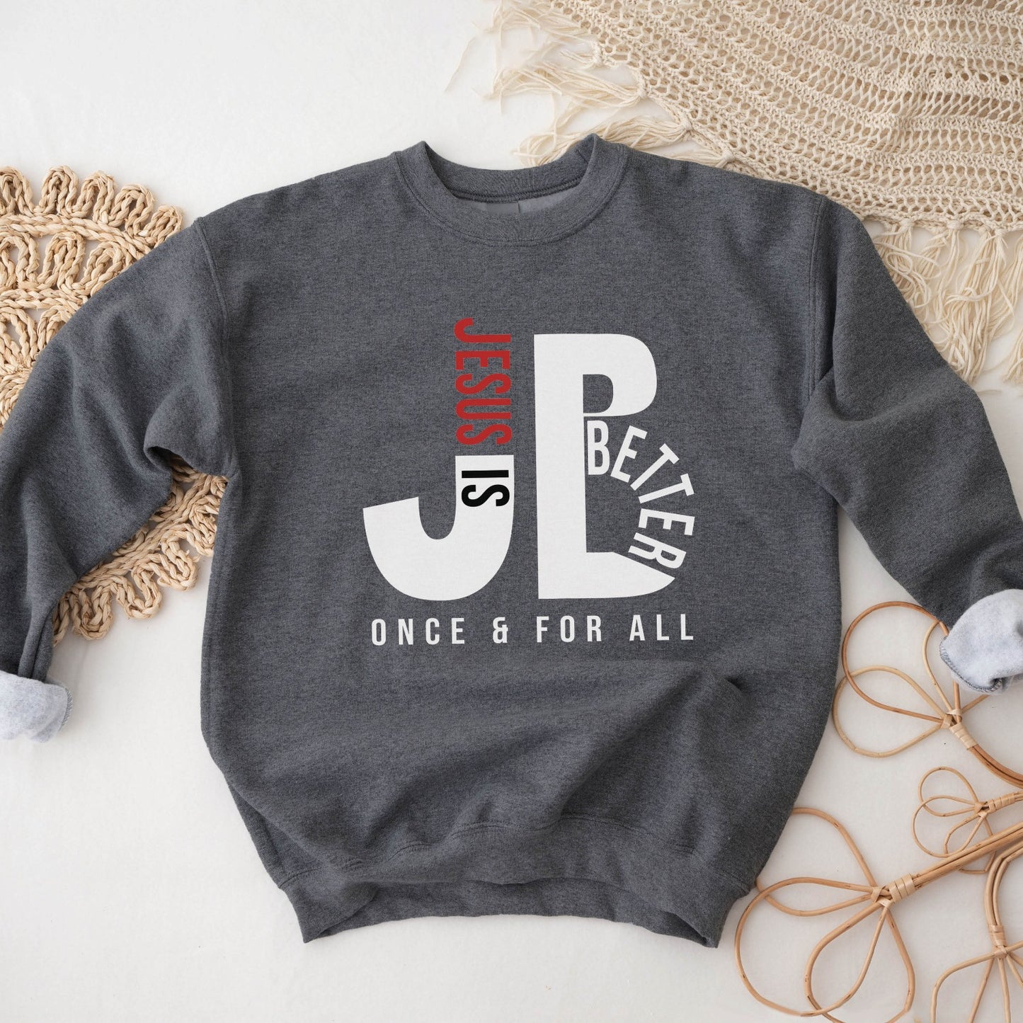 Cozy "JB" typography "Jesus is Better Once and For All" design in white and red letters, based on the Christian bible book of Hebrews, printed on a heather dark gray color Unisex crewneck sweatshirt, created for faith-based men and women