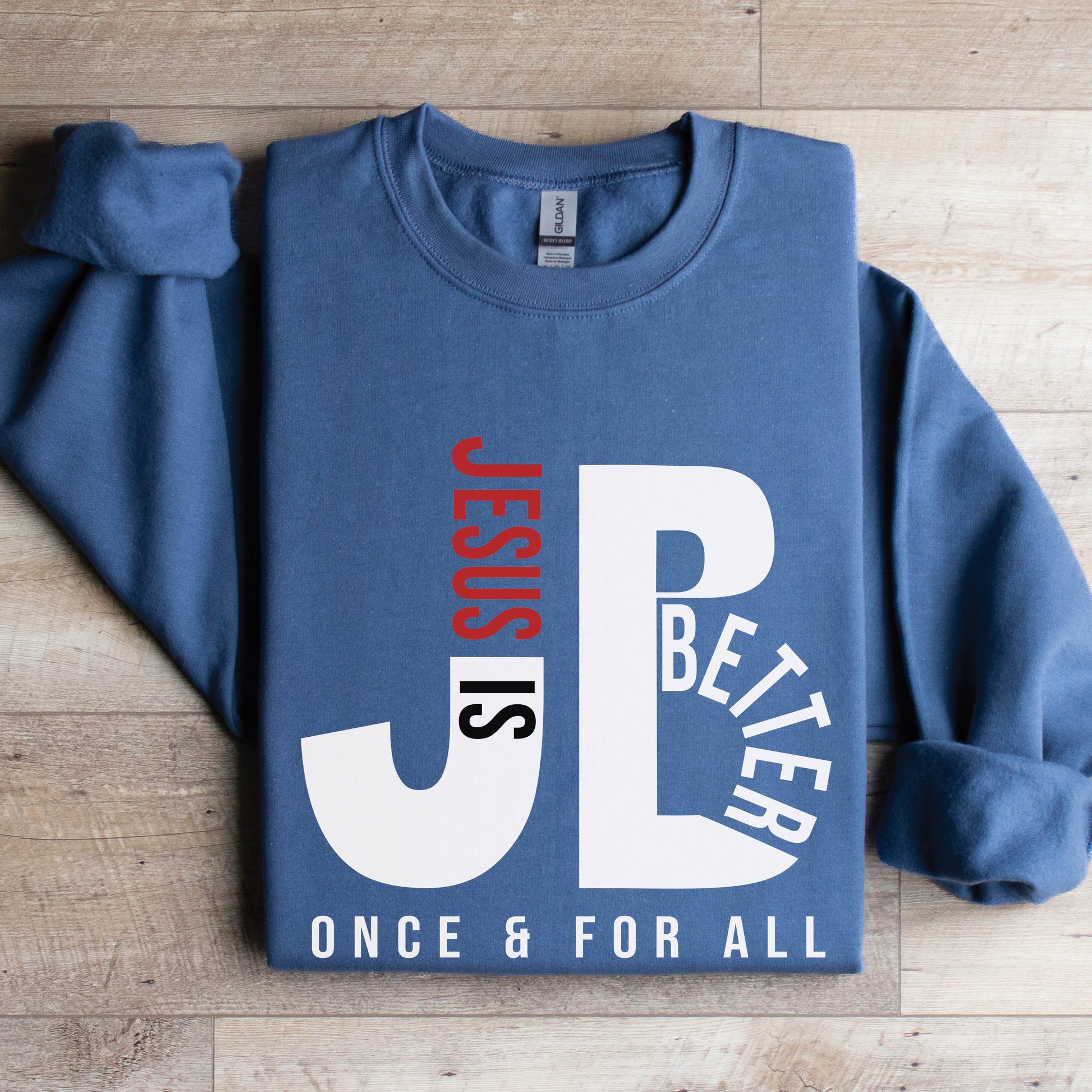 Cozy "JB" typography "Jesus is Better Once and For All" design in white and red letters, based on the Christian bible book of Hebrews, printed on a indigo blue color Unisex crewneck sweatshirt, created for faith-based men and women