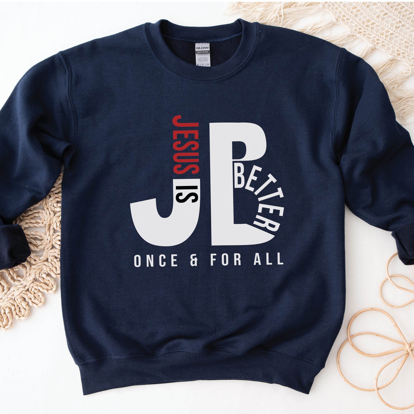 Cozy "JB" typography "Jesus is Better Once and For All" design in white and red letters, based on the Christian bible book of Hebrews, printed on a navy blue color Unisex crewneck sweatshirt, created for faith-based men and women, great father's day gift for dad