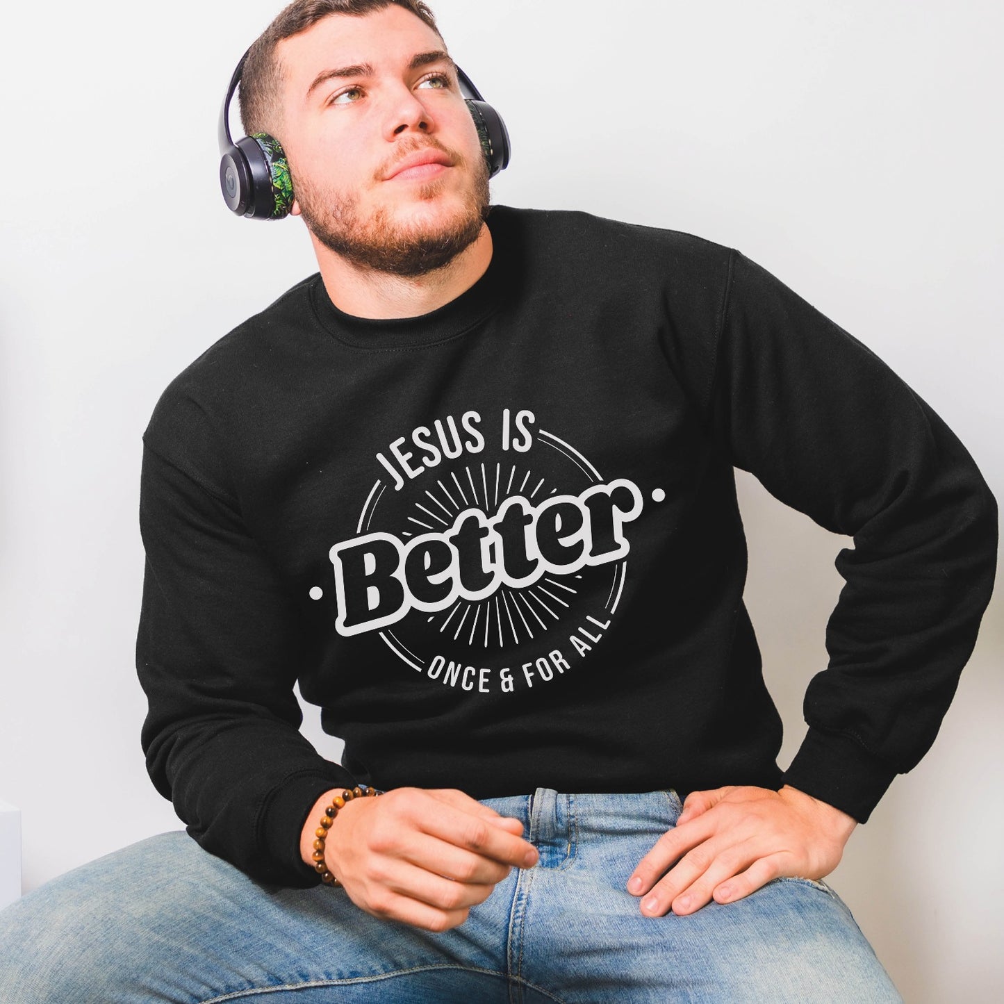 Man wearing a black faith-based cozy sweatshirt with "Jesus is BETTER - Once and For All" logo style design in white, created for Christian men and women