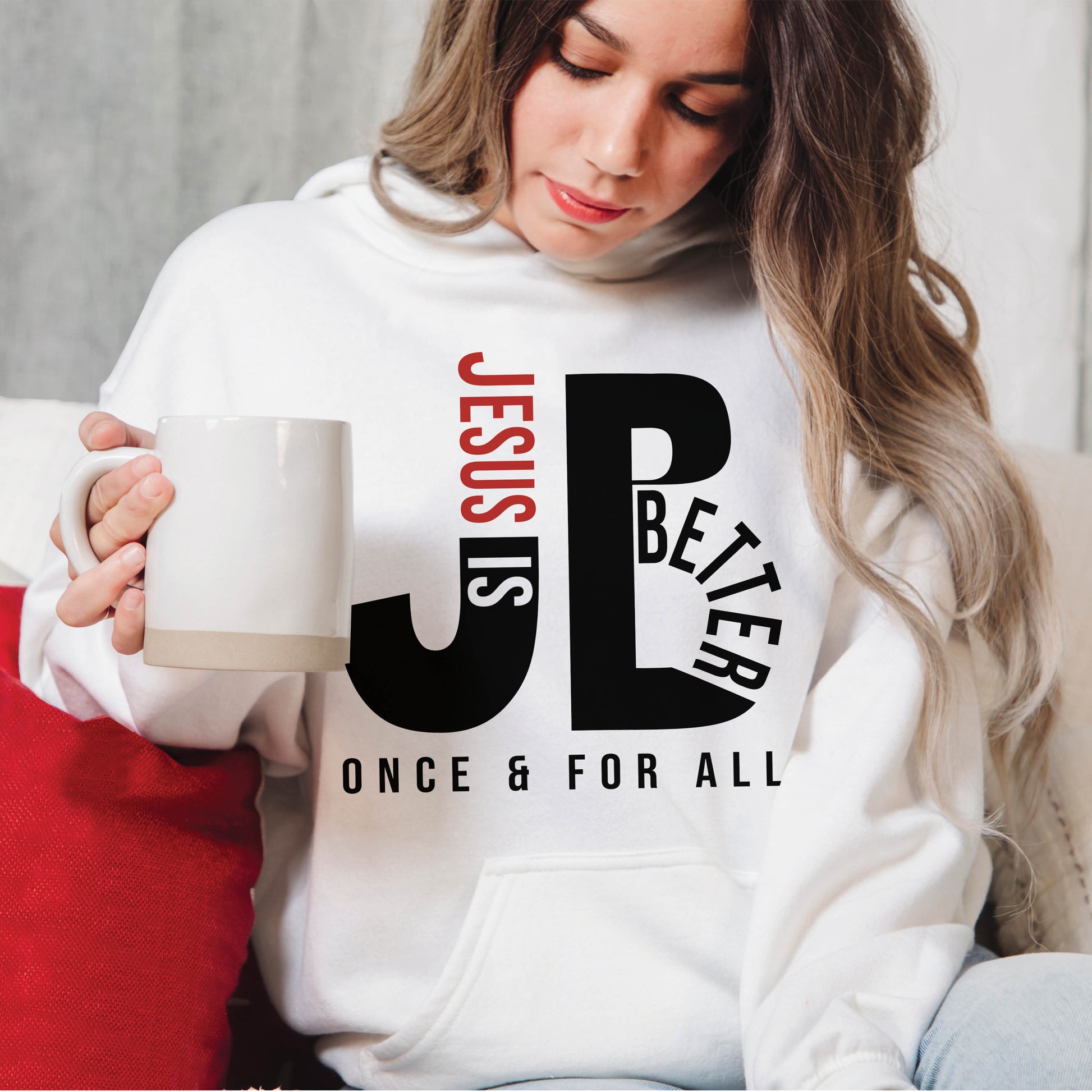 Woman like a Mom wearing a cozy "JB" typography "Jesus is Better Once and For All" design in black and red letters, based on the Christian bible book of Hebrews, printed on a white color unisex hoodie, created for faith-based men and women, great mother's day gift for her