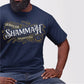 Strong black Christian man wearing a Jehovah Shammah "The Lord Is There" unisex navy blue t-shirt from Ezekiel 38:35 vision bible verse Hebrew meaning, with vintage blackletter and ornate gold decorative swirl filigree design, created for men and women believers