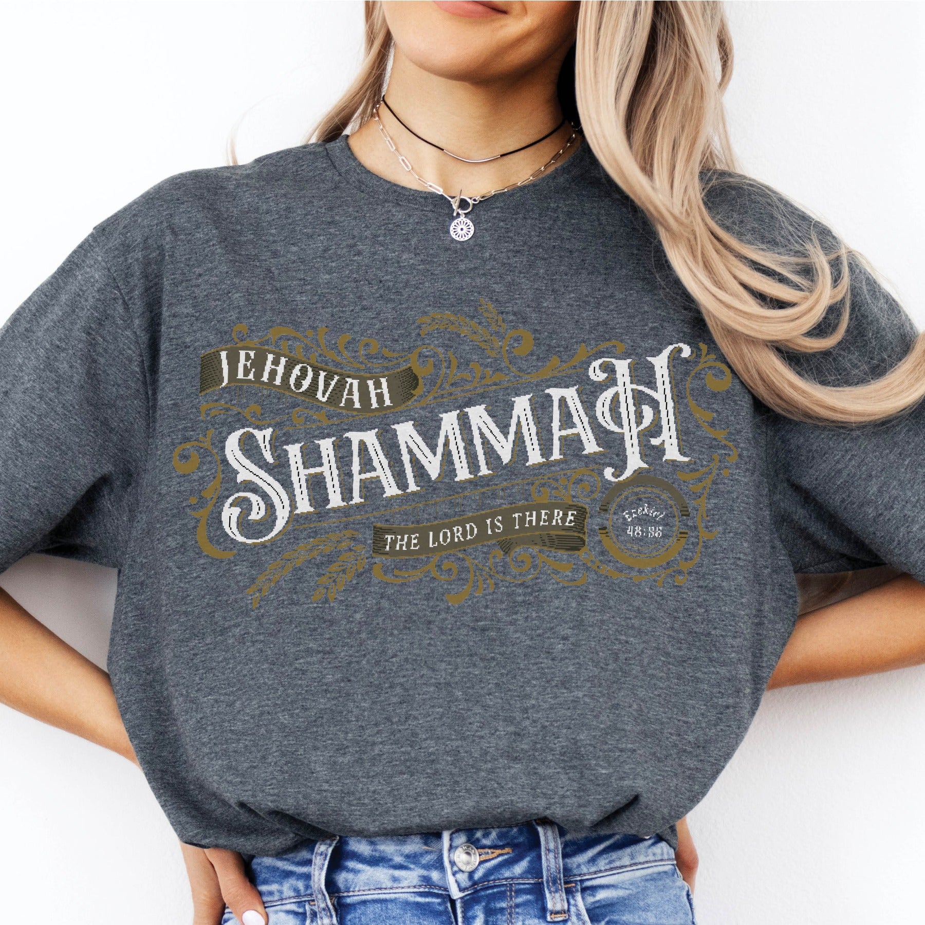 Young woman wearing a Jehovah Shammah "The Lord Is There" soft unisex heather dark gray Christian t-shirt from Ezekiel 38:35 vision bible verse Hebrew meaning, with vintage blackletter and ornate gold decorative swirl filigree design, created for men and women Jesus believers