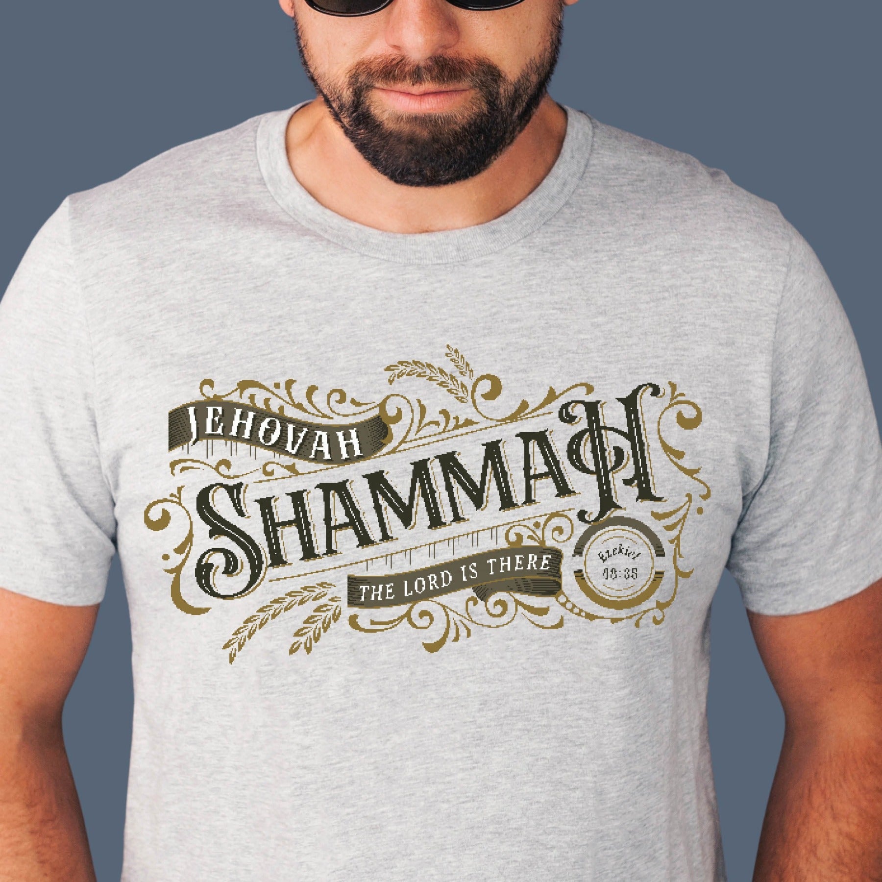 Christian man wearing a Jehovah Shammah "The Lord Is There" soft unisex heather gray t-shirt from Ezekiel 38:35 vision bible verse Hebrew meaning, with vintage blackletter and ornate gold decorative swirl filigree design, created for men and women Jesus bible believers