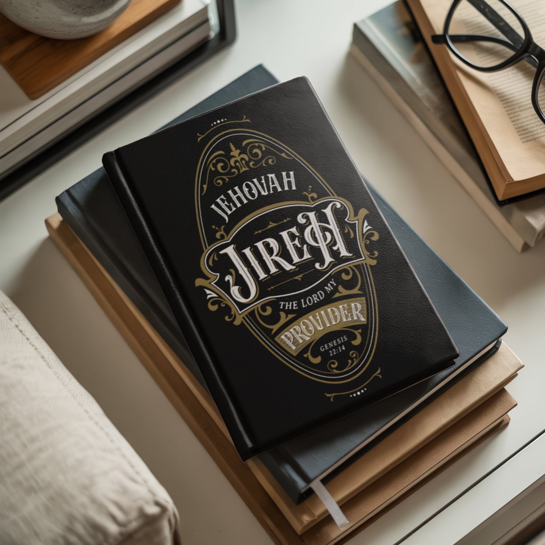 Black Christian prayer journal lined notebook with gold and white vintage blackletter oval ornate frame design with Jehovah Jireh The LORD My Provider Genesis 22:14 bible verse printed on the front and back sides, laying on top of a stack of books