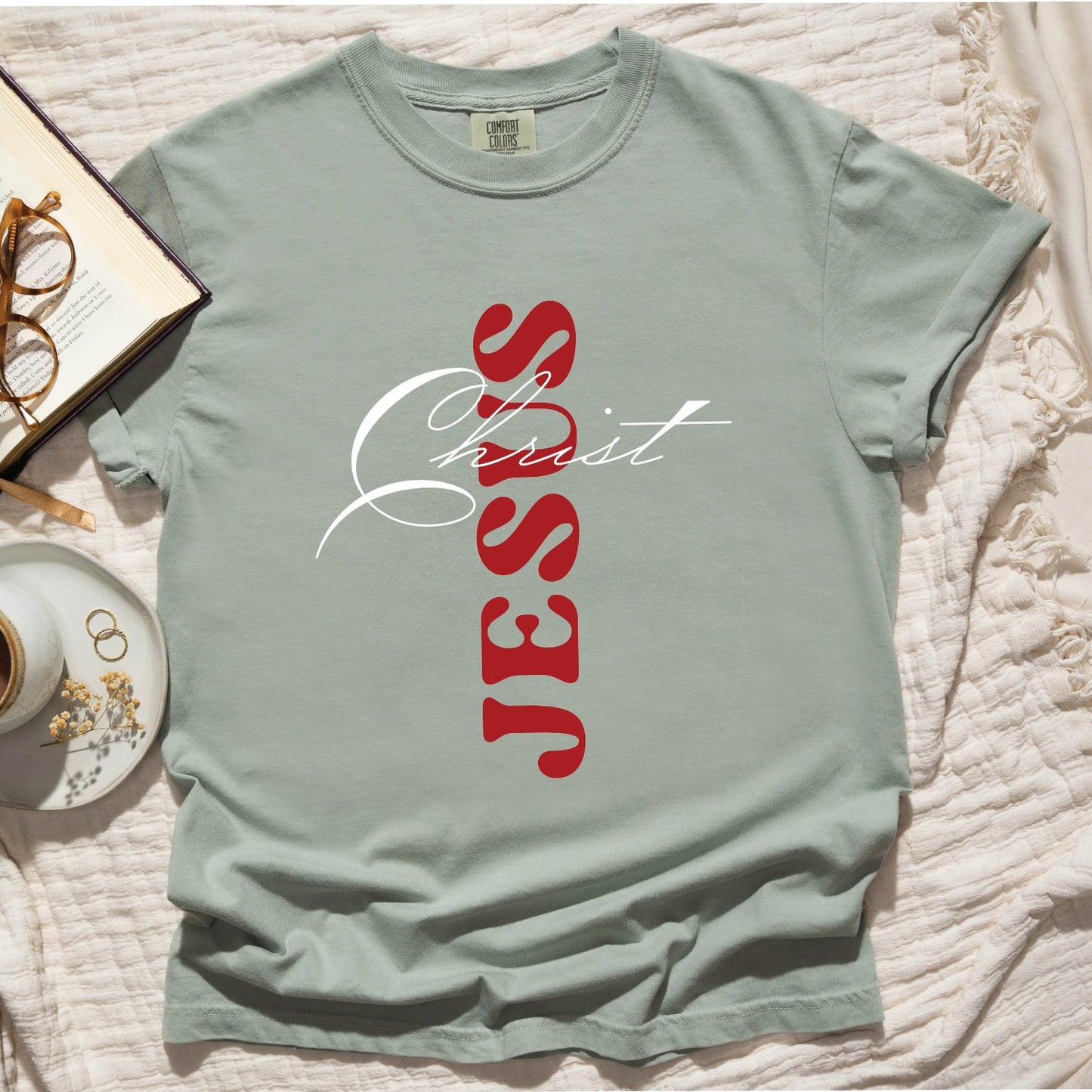 Bay sage green color Christian Comfort Colors 1717 heavyweight unisex t-shirt with faith-based bible typography that says, "Jesus Christ" and white and red letters in the shape of the cross, created for men and women Kingdom believers