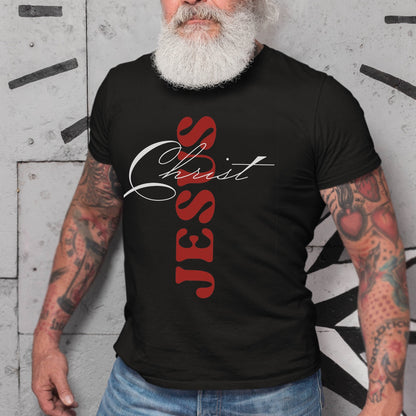 Edgy Tattoo Man wearing a Black color Christian Comfort Colors 1717 heavyweight unisex t-shirt with faith-based bible typography that says, "Jesus Christ" and white and red letters in the shape of the cross, created for men and women Kingdom believers