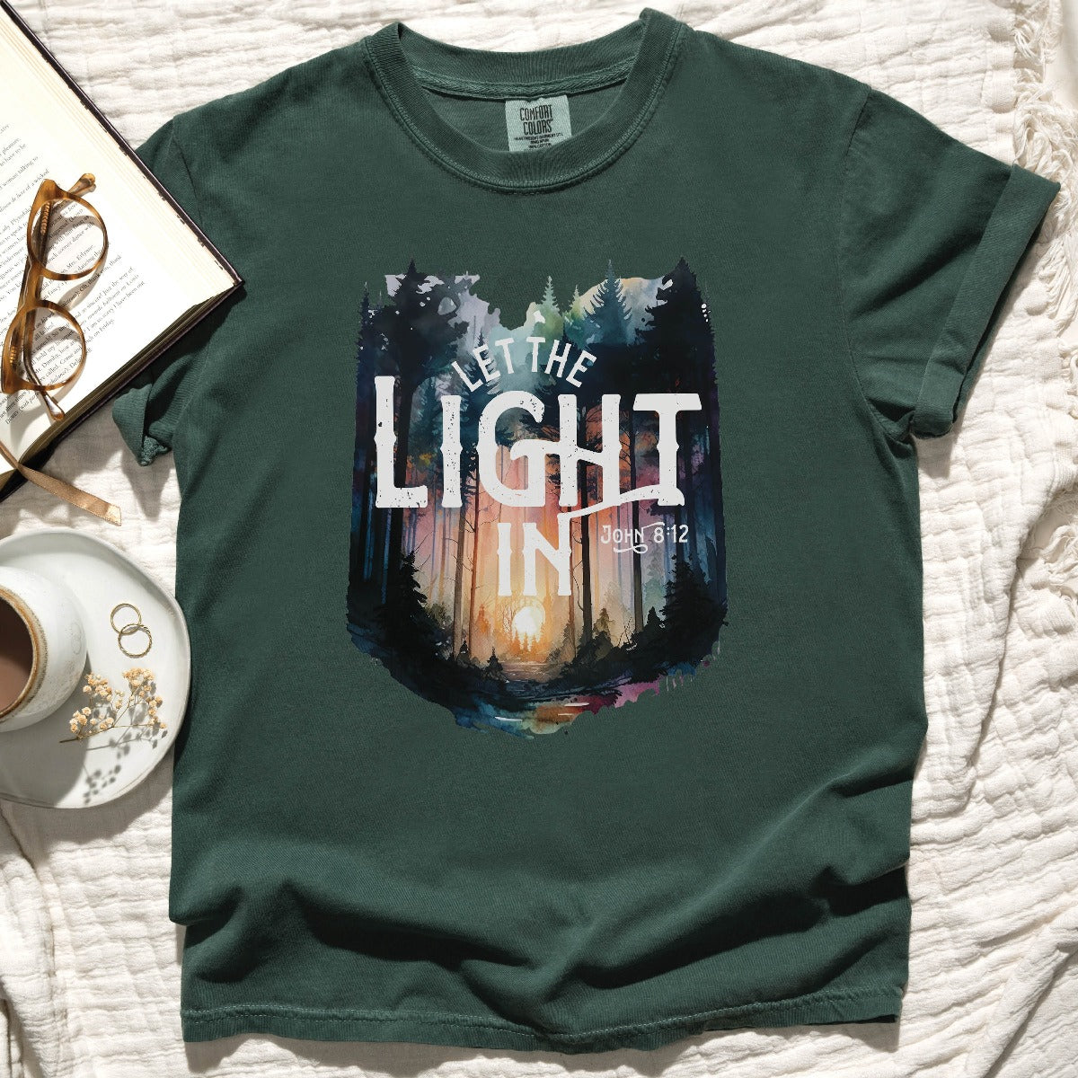 Blue Spruce dark green color garment dyed Comfort Colors C1717 unisex faith-based Christian t-shirt with "Let the Light In" John 8:12 bible verse and watercolor moody forest trees scene, designed for men and women