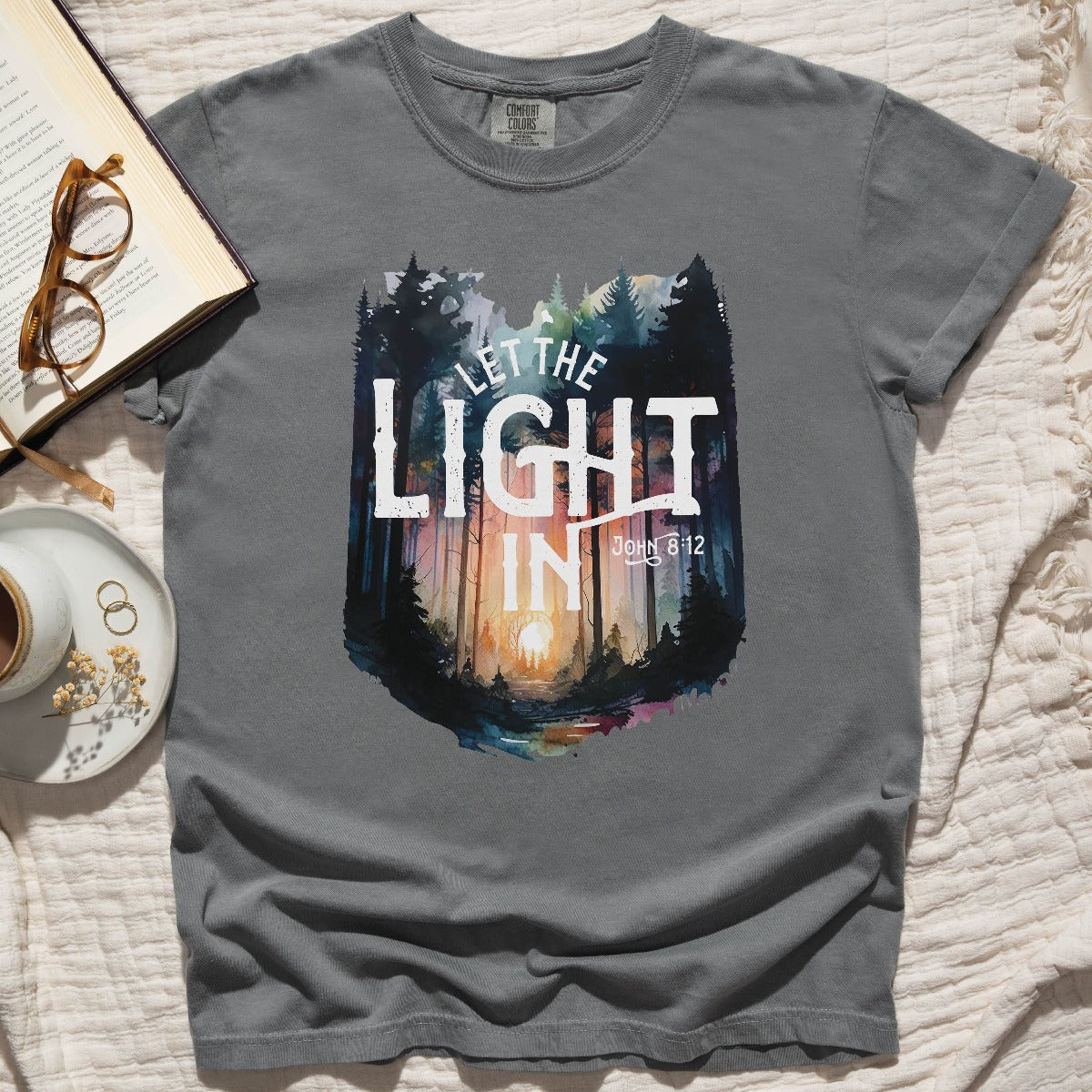 Distressed gray garment dyed Comfort Colors C1717 unisex faith-based Christian t-shirt with "Let the Light In" John 8:12 bible verse and watercolor moody forest trees scene, designed for men and women