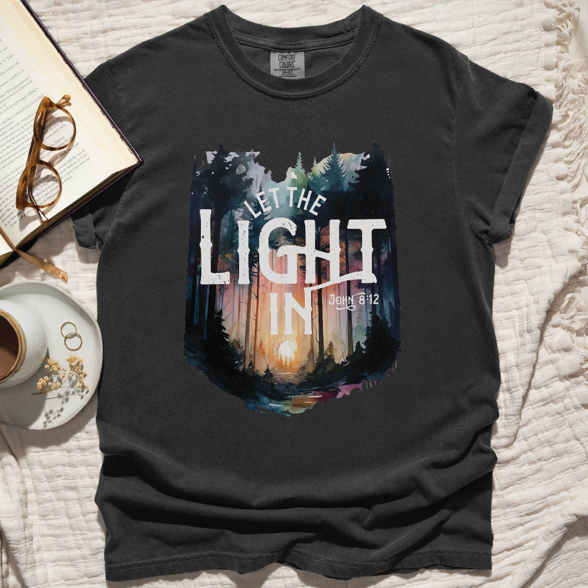 Pepper distressed black Comfort Colors C1717 unisex faith-based Christian t-shirt with "Let the Light In" John 8:12 bible verse and watercolor moody forest trees scene, designed for men and women