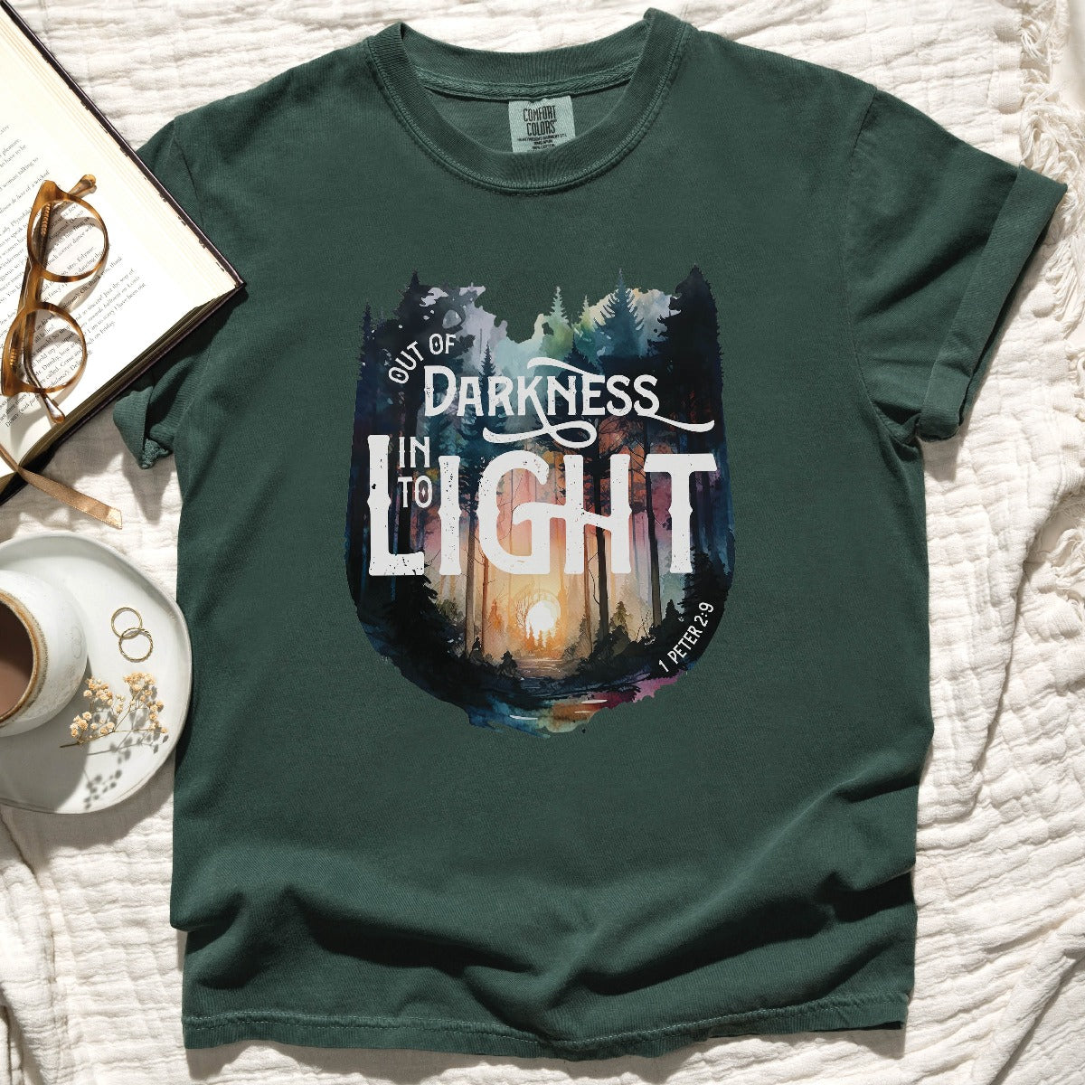 Blue Spruce dark green color garment dyed Comfort Colors C1717 unisex faith-based Christian t-shirt with "Out of Darkness, Into Light" 1 Peter 2:9 bible verse and watercolor moody forest trees outdoor scene, designed for men and women