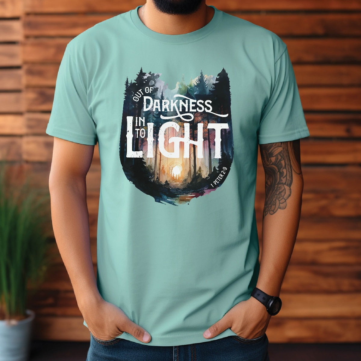 Bearded trendy man wearing Seafoam bright teal color garment dyed Comfort Colors C1717 unisex faith-based Christian t-shirt with "Out of Darkness, Into Light" 1 Peter 2:9 bible verse and watercolor moody forest trees outdoor scene, designed for men and women