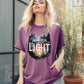 Woman wearing a Berry soft violet purple color garment dyed Comfort Colors C1717 unisex faith-based Christian t-shirt with "Out of Darkness, Into Light" 1 Peter 2:9 bible verse and watercolor moody forest trees outdoor scene, designed for men and women