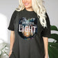 Young beautiful lady wearing a Pepper distressed black color garment dyed Comfort Colors C1717 unisex faith-based Christian t-shirt with "Out of Darkness, Into Light" 1 Peter 2:9 bible verse and watercolor moody forest trees outdoor scene, designed for men and women
