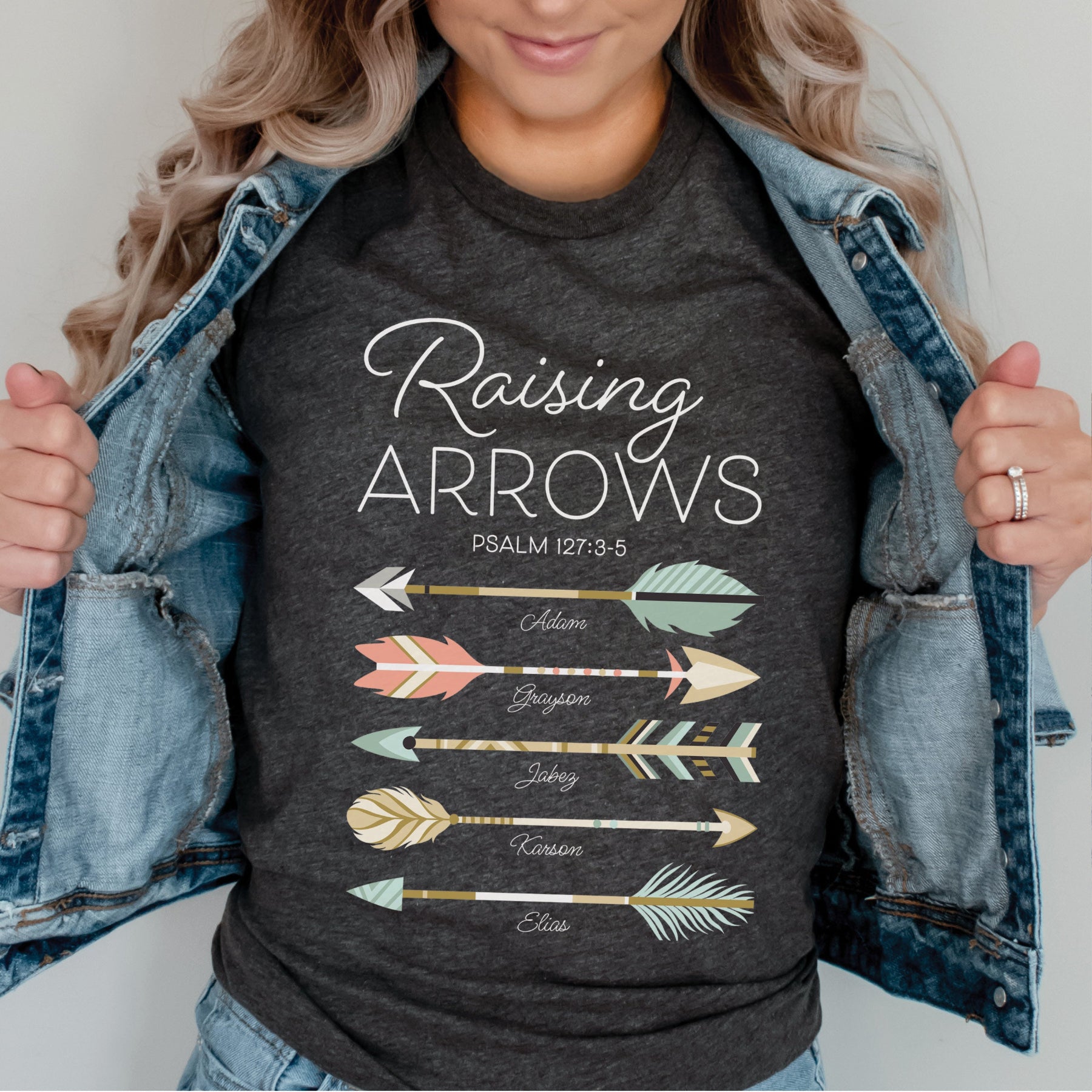 Christian mom young woman wearing a dark heather gray t-shirt with 'Raising Arrows' Psalm 127:3-5 design with 5 personalized names under each arrow on a white background