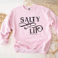 Faith-based "Salty And Lit Matthew 5:13-14" bible verse funny Christian aesthetic unisex crewneck sweatshirt with distressed swirl typography design printed in charcoal gray on cozy girly pink sweater for women