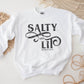 Salty And Lit Matthew 5:13-14 bible verse funny Christian aesthetic unisex crewneck sweatshirt with distressed swirl typography design printed in charcoal gray on cozy white sweater for women