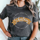 Young woman wearing a soft heather dark gray faith-based Christian women's unisex t-shirt with a gold banner and sunburst design that says the Biblical Hebrew meaning of the word "SHALOM" - Peace, Completeness, Prosperity, Health, Safety, Wholeness, Soundness, and Permanence definition, makes a great mother's day gift for mom!