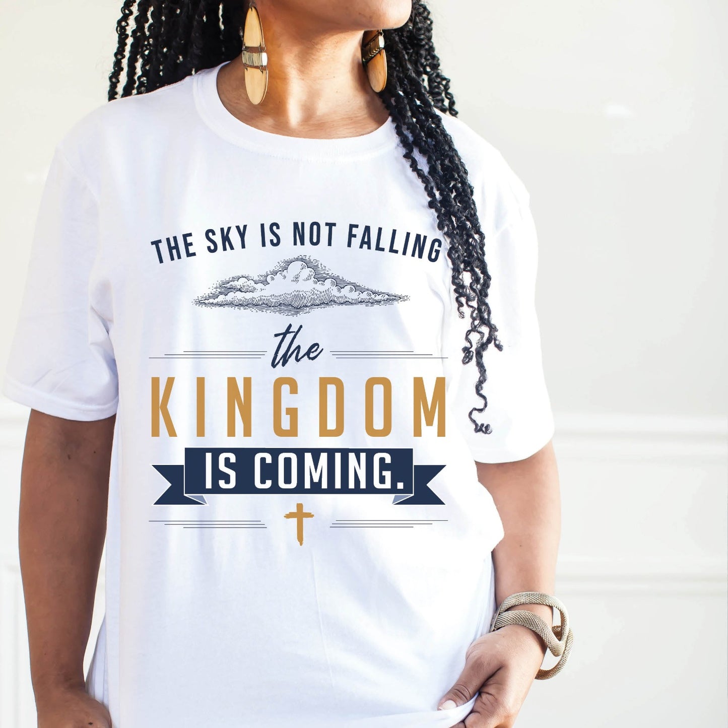 Black woman wearing a unisex t-shirt with a Christian Kingdom of God through Jesus faith-based message that says, "The Sky Is Not Falling, The Kingdom is Coming" with bold font, vintage clouds, banner, and cross design in navy blue and gold, created for bible study Men and Women believers, 2024 eclipse